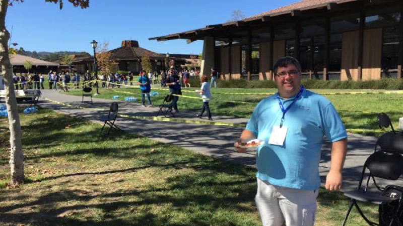 A smiling attendee on a lawn with a long line of people behind.